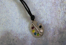 Load image into Gallery viewer, Artist palette pendant necklace on black cord, with painted paint sports, for unisex teen or adult. (photo taken on a low lite background)