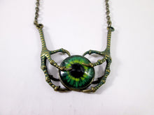 Load image into Gallery viewer, A gothic-style necklace featuring a green and black eye cabochon pendant held by two antique bronze claw-like hands, suspended from a matching chain on a plain white background.