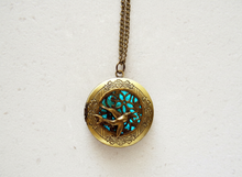 Load image into Gallery viewer, Glow in the dark bird locket necklace in antique bronze, glowing blue.