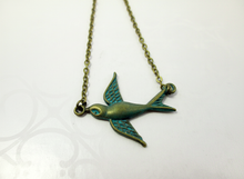 Load image into Gallery viewer, A vintage-style metal bird pendant necklace with a bronze finish and turquoise-blue patina on the wings and eye, hanging on a matching chain against a white background.