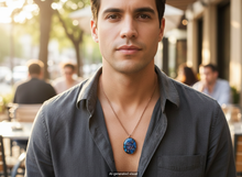 Load image into Gallery viewer, Man wearing a handmade oval copper energy pendant necklace with blue semi-precious stones, pearls and double spiral charm, styled casually outdoors.  A small "AI-generated visual" label is shown at the bottom.