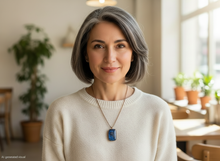 Load image into Gallery viewer, Woman with gray hair wearing a handmade rectangular copper energy pendant necklace with blue semi-precious stones, pearls and double spiral charm, styled casually indoors.  A small "AI-generated visual" marked at the bottom left hand corner.