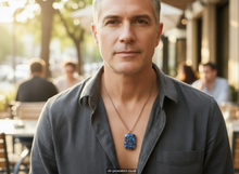 Load image into Gallery viewer, Man with gray hair wearing a handmade rectangular copper energy pendant necklace with blue semi-precious stones, pearls and double spiral charm, styled casually outdoors.  A small "AI-generated visual" label is shown at bottom.