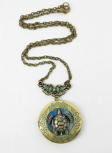Load image into Gallery viewer, An antique bronze locket necklace featuring a detailed sea turtle pendant with blue and pink enamel accents, displayed on a clean white background.