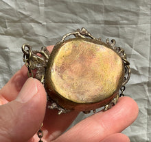 Load image into Gallery viewer, A close-up of a hand holding a pendant with copper back against a wrinkled light gray fabric background.  
