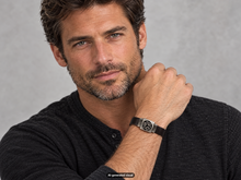 Load image into Gallery viewer, Male model wearing the Traveler's Protection Celtic Nehalennia Goddess Bracelet, featuring a hand‑cast pewter centerpiece on a black leather band, shown against a neutral gray background.  A small label "AI-generated visual" appears at the bottom of the photo.