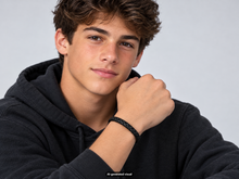 Load image into Gallery viewer, Male model in a black hoodie displaying a black leather braided bracelet with a raised hand against a light gray background.  A small "AI generated visual" label appears at the bottom of the photo.