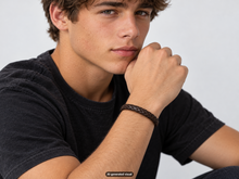 Load image into Gallery viewer, Male model wearing a brown leather braided bracelet with a short‑sleeve dark shirt against a light background.  A small "AI-generated visual" label appears at the bottom of the photo.