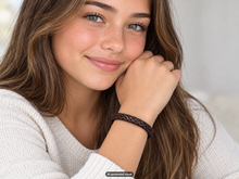 Load image into Gallery viewer, Female model wearing a dark brown leather braided bracelet while resting her chin on her hand, shown in soft indoor lighting.  A small "AI generated visual" label appears at the bottom of the photo.