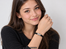 Load image into Gallery viewer, Female model in a black sweater showcasing a black leather braided bracelet with a silver color clasp against a light background.  A small "AI generated visual" label appears at the bottom of the photo.