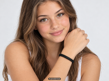 Load image into Gallery viewer, Female model wearing a black leather braided bracelet while resting her chin on her hand, shown against a light neutral background.  A small "AI generated visual" label" appears at the bottom of the photo.