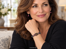 Load image into Gallery viewer, Female model wearing a red abalone shell magnetic hematite bracelet with pink rhinestone accents, shown in a warm, cozy indoor setting.  A small "AI-generated" visual label appears at the bottom of the image.