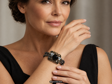 Load image into Gallery viewer, Close-up of a model showcasing an antique bronze and black magnetic hematite bracelet with ornate detailing.  A small "AI-generated visual" label appears at the bottom of the image.