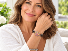Load image into Gallery viewer, Model wearing a pink flower magnetic hematite bracelet with a decorative rectangular floral centerpiece, shown in a soft indoor setting.  A small "AI-generated visual" label appears at the bottom of the image.