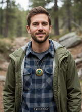 Load image into Gallery viewer, A man wearing a green hooded jacket over a blue and gray plaid flannel shirt, with a bronze tone blue glowing bird locket necklace, standing outdoors in a blurred forest setting.  A small "AI-generated visual" appears at the bottom .