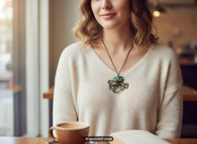 Load image into Gallery viewer, A woman wearing a cream-colored knit sweater and a bronze owl octopus pendant necklace glowing blue in the dark, seated at a table with a coffee cup in a cafe setting.  A small "AI-generated visual" label appears at the bottom.
