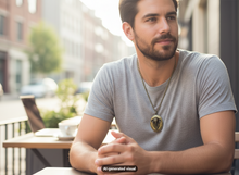 Load image into Gallery viewer, A man with a beard wearing a gray t-shirt and a bronze elephant locket necklace sits at an outdoor cafe table. The image has a visible 'AI-generated visual' watermark at the bottom.