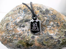 Load image into Gallery viewer, close-up front view of handmade pewter paddler pendant necklace, pendant with black background, on black cord, for men or women (photo of necklace taken on a background with a rock)