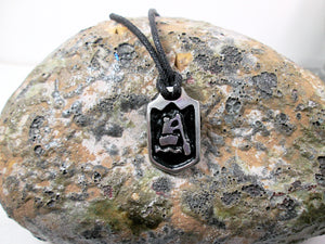 close-up front view of handmade pewter paddler pendant necklace, pendant with black background, on black cord, for men or women (photo of necklace taken on a background with a rock)