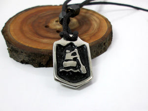 close-up front view of handmade pewter paddler pendant necklace, pendant with black background, on black cord, for men or women (photo of necklace taken on a background with a piece of wood)