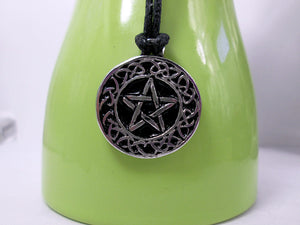 Celtic pentacle pendant necklace, round pendant with black background, on black cord, for unisex teen or adult. (photo taken on a green background)