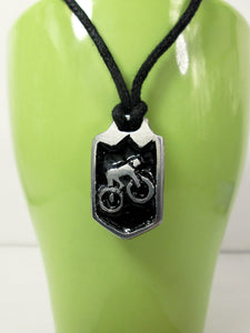 cycling pendant necklace, biker pendant necklace, pendant with black background, on black cord, for unisex teen or adult. (photo taken on a green background)