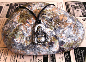 handmade pewter happy laughing buddha pendant necklace, for men or women, on black cord. (photoof necklace taken on a background with a piece of rock)