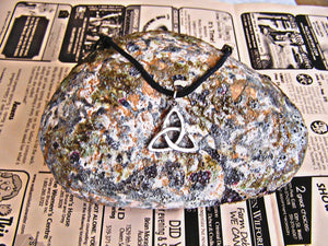 front view of Celtic Trinity Knot pendant necklace, on black cord, for unisex teen or adult. (photo taken on a background with a rock)