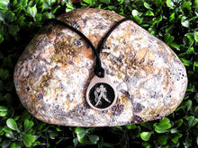 Load image into Gallery viewer, Aquarius horoscope pendant necklace on black cord with black background, teardrop shaped, for man or woman. (photo taken on a rock background.)