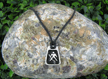 Load image into Gallery viewer, handmade pewter hockey goalie pendant necklace, polygon pendant with black background, for men or women, on black cord. (photo taken of necklace on a background with a rock)