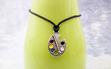 Load image into Gallery viewer, Artist palette pendant necklace on black cord, with painted paint sports, for unisex teen or adult. (photo taken on a green background)