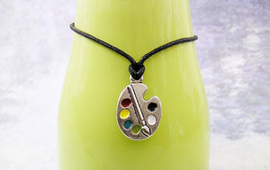 Artist palette pendant necklace on black cord, with painted paint sports, for unisex teen or adult. (photo taken on a green background)